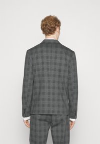Grijze geblokte blazer van gestructureerde stof, met een sluiting met twee knopen, verwonding van de revers en knoopmanchetten. Achteraanzicht weergegeven.