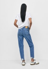 Jeans de mezclilla azul claro con un corte relajado, detalles desgastados en el dobladillo, combinados con una camiseta blanca y zapatillas en blanco y negro.