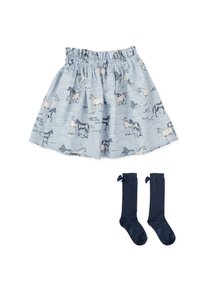 Jupe bleu clair avec des imprimés de chevaux, taille élastique et ourlet volanté. Associée à des chaussettes montantes bleu marine ornées de nœuds.