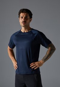 Marinefarbene sportliche T-Shirt aus weichem, feuchtigkeitsableitendem Stoff; mit Raglanärmeln und fitted Design, einer glatten Textur und minimalen Nähten.