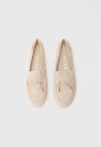 Μπεζ μοκασίνια από σουέτ με δεμένη φιόγκο και χρυσούς μεταλλικούς τόνον. Διαθέτουν λεία υφή και διακοσμητικό ράψιμο κατά μήκος των άκρων.