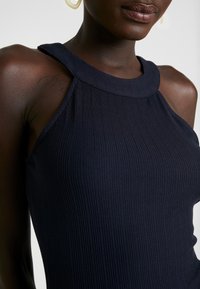 Marinblå ribbad linne med hög halsringning och breda axelband, som har en figurnära silhuett och en slät textur.