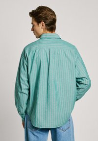 Camicia a maniche lunghe in tessuto leggero a righe verdi; presenta un colletto classico, maniche lunghe e un retro plissettato per una maggiore libertà di movimento.