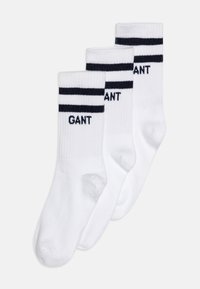 Vita bomullssockor med marinblå ränder, med "GANT"-logotyp i marinblå text. Tre par visas, vilket visar ribbat mönster och medellång längd.