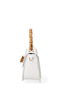 Borsa a mano in pelle bianca con manico in bamboo, dettagli hardware dorati e forma trapezoidale. Presenta un anello metallico decorativo sul lato.