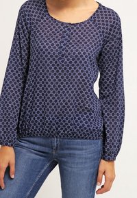 Marinblus med lång ärm, cirkulära mönster, rundad halsringning och knappar framtill.