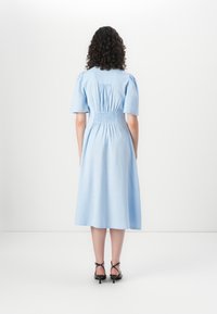 Rochie de lungime până la genunchi, de culoare albastru deschis, cu mâneci bufante, spate elastic și croială în formă de A. Purtați cu sandale negre cu bretele. Textură de țesătură netedă.