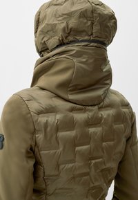 Olijfgroene pufferjack met een gestructureerd quiltpatroon, geïsoleerde capuchon en gladde stofaccenten op de schouders. Voorzien van een logo-opdruk.