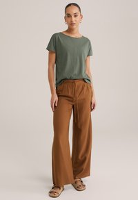 Zaļš, īsām piedurknēm T-krekliņš ar brīvu piegriezumu, kombinēts ar brūniem, plašiem biksēm ar savilkšanas jostu un teksturētu audumu. Beigžu sandalītes.