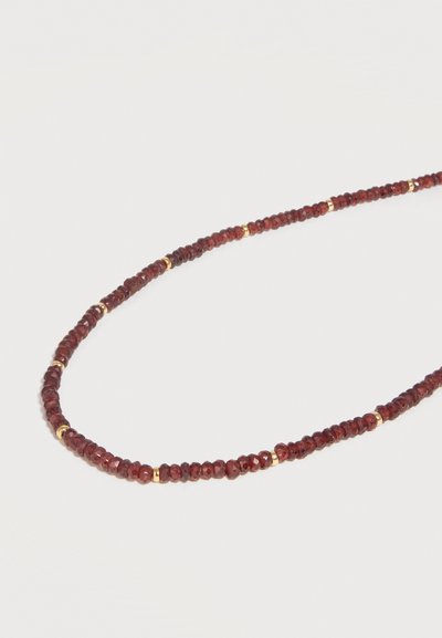 Λεπτό κολιέ με μικρές σκαλιστές σκούρες κόκκινες χάντρες εναλλάσσονται με μικρές χρυσές διαχωριστικές χάντρες σε ανοιχτό φόντο.