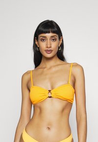 Gul topp i bikinitype med samlet design, som har en rund utskjæring i midten og tynne justerbare stropper. Teksturert stoff.