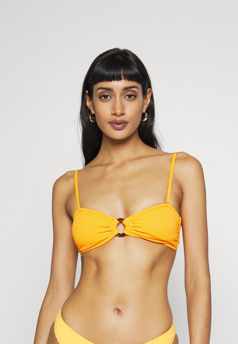 Gul topp i bikinitype med samlet design, som har en rund utskjæring i midten og tynne justerbare stropper. Teksturert stoff.