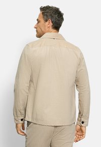 Beige Cord-Jacke mit vertikalen Streifen. Verfügt über einen Kragen, eine knopffixierte Manschette und einen geraden Schnitt. Die Rückansicht zeigt die Nahtdetails und die Textur.