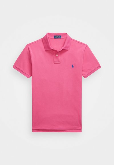 Rozā polo krekls, izgatavots no kokvilnas, īsām piedurknēm, ar apkakli, divu pogu slēgšanu. Ir izšūta zila emblēma kreisajā krūtī.