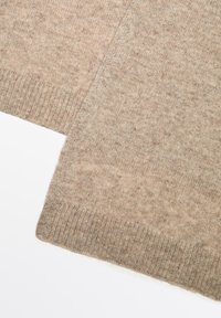 Écharpe en laine beige avec un motif tricoté texturé. Les bords sont côtelés, offrant un contraste subtil avec la surface douce et lisse.