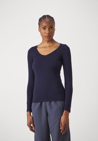 Marineblauwe long sleeve top met een V-hals en een aansluitend ontwerp, gemaakt van gladde stof met minimale naden en een logo-detail aan de zoom.