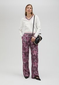 White V-neck sweatshirt with colored stripes at the neck and hem, paired with pink leopard print wide-leg pants. Black bag with chain strap.