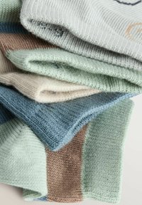 Cinq chaussettes pliées de couleurs variées : gris, vert clair, beige, bleu et marron. Elles présentent une texture côtelée et un tissu doux.