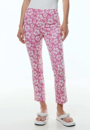 Rosa, floral gemusterte Hose mit figurnaher Passform, mittelhohem Bund und dehnbarem Stoff. Kombiniert mit weißen Plateausandalen.