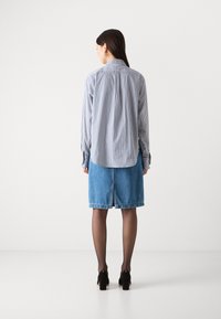 Randig skjorta i blått och vitt med långa ärmar, i kombination med en denimkjol. Svarta klackskor och genomskinliga svarta strumpbyxor fulländar outfiten.