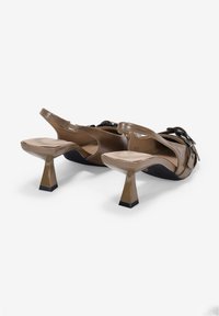 Sandales en cuir verni marron avec un dos ouvert, des talons carrés épais et des accents noirs. Elles possèdent des brides de cheville ajustables et une texture lisse.