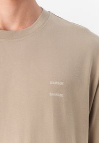 Lysebrun langærmet t-shirt lavet af blødt stof. Har to "SAM Sø" logoer i hvid på venstre side af brystet.