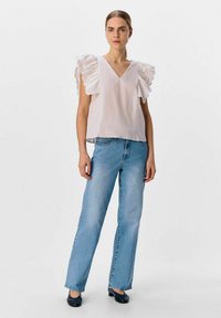 Weißes V-Ausschnitt-Oberteil mit Rüscheärmel, kombiniert mit hellblauen geraden Jeans und schwarzen Schuhen. Einfaches Design, glatte Textur, lässiger Look.