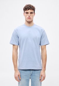 Világoskék pamut póló rövid ujjakkal, kerek nyakkivágással és diszkrét logóval az elején. Egyszerű, laza szabású design.