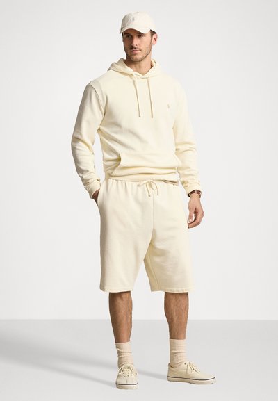 Ljusgul huvtröja med ficka fram, i kombination med matchande shorts. Bärs med krämfärgade sneakers och keps. Strukturerad textil.
