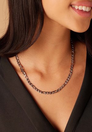 Collier en chaîne en argent avec des maillons ovales présentant des surfaces lisses et texturées alternées. Porté autour du cou sur un haut noir.