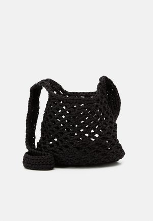 Schwarze gehäkelte Schultertasche mit offenem Gewebemuster und einem breiten Riemen, vor einem schlichten hellen Hintergrund platziert.