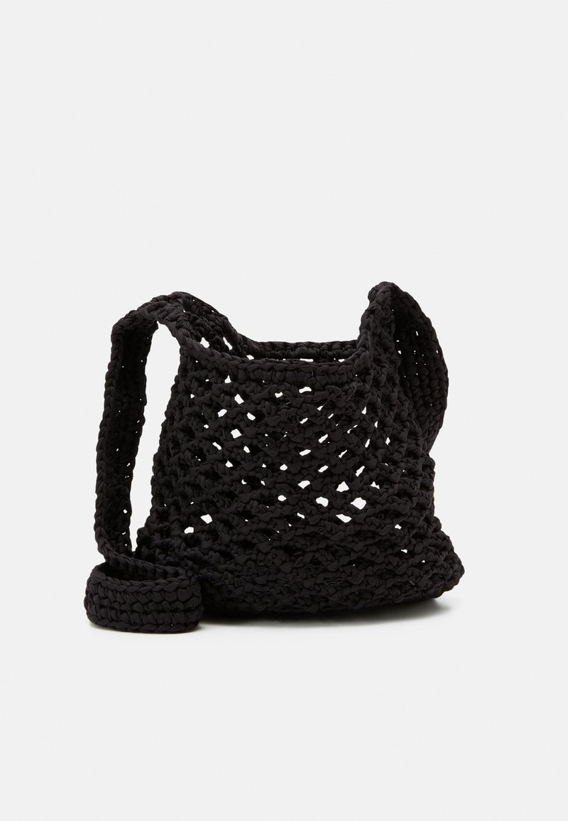 Sac d’épaule noir crocheté avec un motif à tissage ouvert et une large bandoulière, placé sur un fond clair uni.