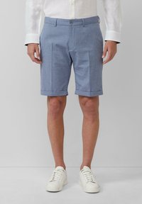 Blaue gemusterte Shorts mit flachem Bund und umgeschlagenen Säumen, aus leichtem Stoff. Kombiniert mit weißen Sneakers und einem hellen Hemd.
