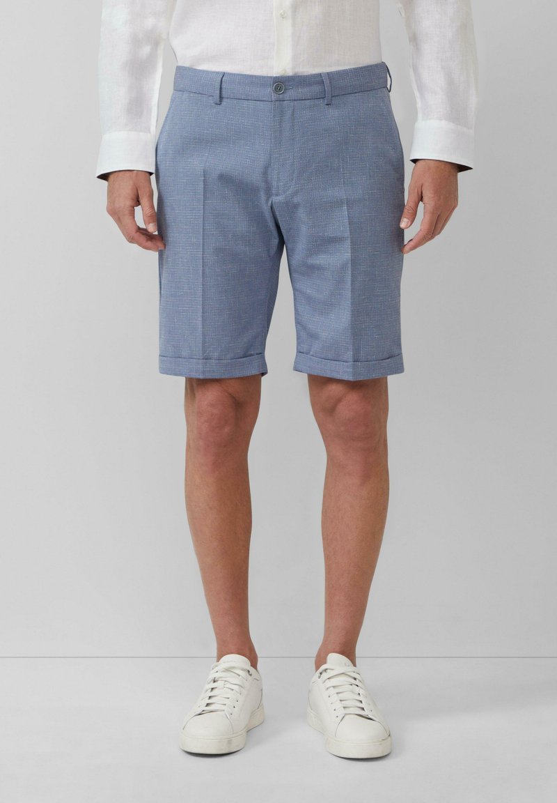Blaue gemusterte Shorts mit flachem Bund und umgeschlagenen Säumen, aus leichtem Stoff. Kombiniert mit weißen Sneakers und einem hellen Hemd.