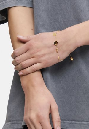 Gold chain bracelet with small circular pendants, thin links, a delicate design, and a lobster clasp closure. Worn on a hand with light skin tone.