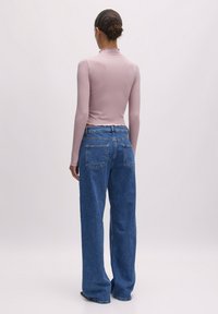 Langärmliges, hellrosa enganliegendes Oberteil mit gewelltem Ausschnitt, kombiniert mit locker sitzenden blauen Jeans aus Denim mit hoher Taille und Gesäßtaschen.