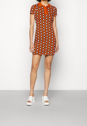 Korte mouws oranje polojurk met een herhalend zwart-wit bloemenpatroon, een kraag en een aangesloten silhouet.