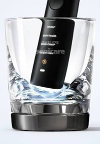 Spazzolino Philips Sonicare in un bicchiere. Manico nero con etichette grafiche per le funzioni. Il bicchiere rivela acqua e una base metallica arrotondata.
