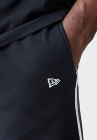 Crne atletske kratke hlače s bijelim vezanim logotipom, bočnim trakama i glatkom teksturom. Struk ima malu džepu.