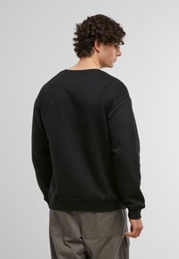 Sort sweatshirt med rund hals, ribbede manchetter og kant, samt en afslappet pasform. Glat tekstur med minimal detaljer, båret med grå cargo bukser.