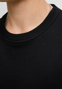 Fekete pamut T-shirt, bordázott kerek nyakkivágással, sima textúrával és testhezálló kialakítással. A nyakkivágás mentén látható varrási részletek.