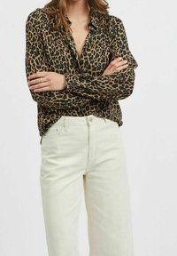 Blůza s leopardím potiskem v odstínech hnědé a černé, přiléhavý střih s límcem, v kombinaci s bílými džíny s vysokým pasem.