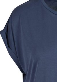 Gros plan d’un t-shirt bleu marine à manches courtes montrant un revers roulé et un col rond sur fond blanc uni.