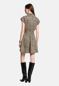 Robe courte à imprimé léopard avec un col, des manches courtes et une taille cintrée, associée à des bottes noires jusqu'aux genoux.