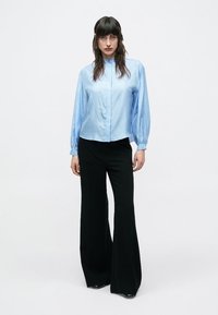 Svetlomodrá košeľa na gombíky s dlhými rukávmi, priliehavým živôtikom a objemnými rukávmi, doplnená čiernymi širokými nohavicami.