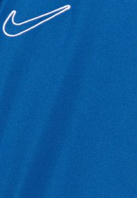 Tela atlética azul con el logo de Nike bordado en blanco. La superficie tiene una textura suave con un ligero brillo.