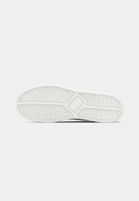 Witte rubberen schoenzool met hexagonaal profielpatroon en het "Tommy Jeans" logo in het midden op een eenvoudige achtergrond.