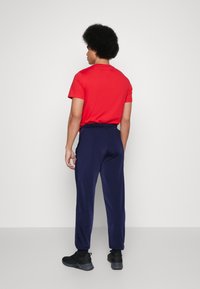 Rød kortærmet t-shirt og marineblå træningsbukser med elastisk talje, parret med sorte sneakers. Enkel, afslappet design.