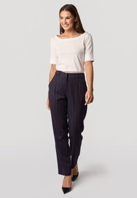 Crème blouse met opgerolde mouwen, gecombineerd met marineblauwe pinstripe broek. De broek heeft zijzakken en een getailleerde pasvorm. Draagt zwarte hakken.