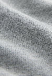 Tejido gris que presenta una suave textura entrelazada con sutiles variaciones en el tono, destacando una apariencia acogedora y relajada.